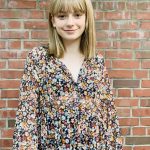 Mädchen mittelblond mit Chiffonkleid millefleurs farblich passend zum Typ. Vor Backsteinwand.